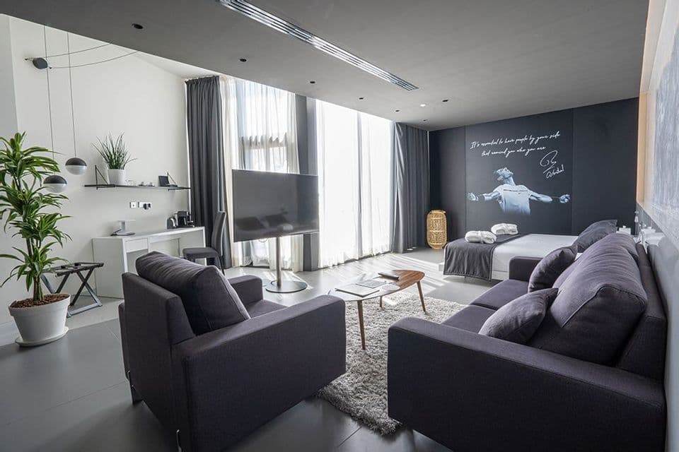 Una suite d'albergo moderna con zona giorno, scrivania e un letto accanto a una parete nera con un murale del tennista Rafael Nadal.