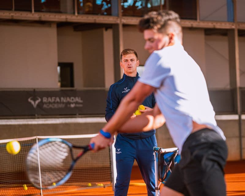 Un tennista colpisce una palla con una racchetta su un campo in terra battuta durante una sessione di allenamento.