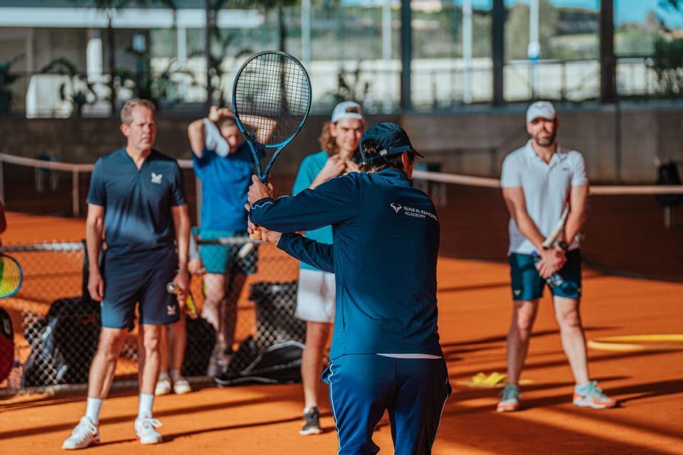 Un gruppo WeRoad riceve lezioni da un maestro di tennis su un campo in terra battuta.