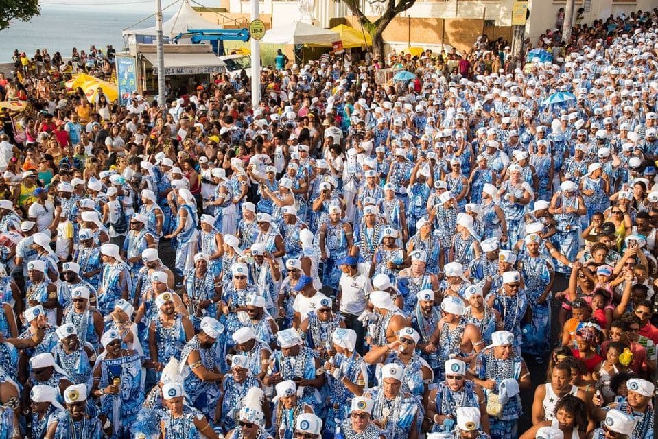 Vue aérienne d'un grand groupe de personnes en costumes bleus et blancs défilant dans une rue bondée.