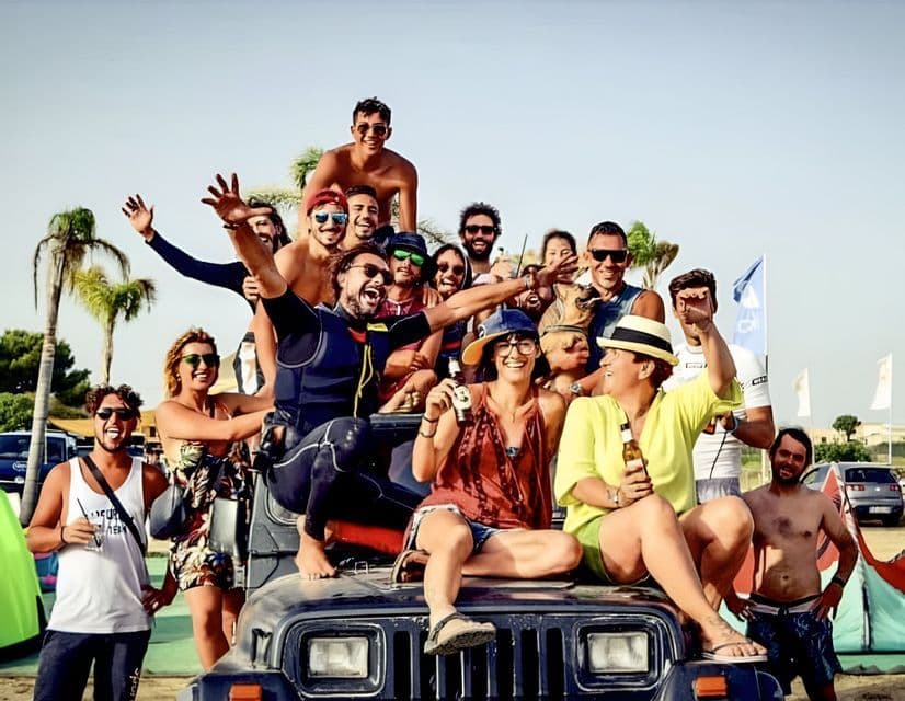 Un viaggio di gruppo WeRoad con persone sorridenti ed esultanti che posano su una jeep scura all'aperto, con palme sullo sfondo.