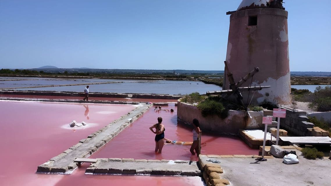 Un viaggio di gruppo WeRoad che fa il bagno nelle saline rosa accanto a un mulino a vento in pietra in una giornata di sole.