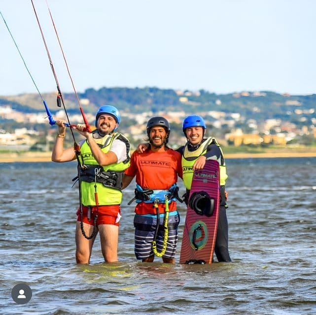 Un viaggio di gruppo WeRoad: tre uomini in caschi e giubbotti di salvataggio posano in acqua con l'attrezzatura da kitesurf.
