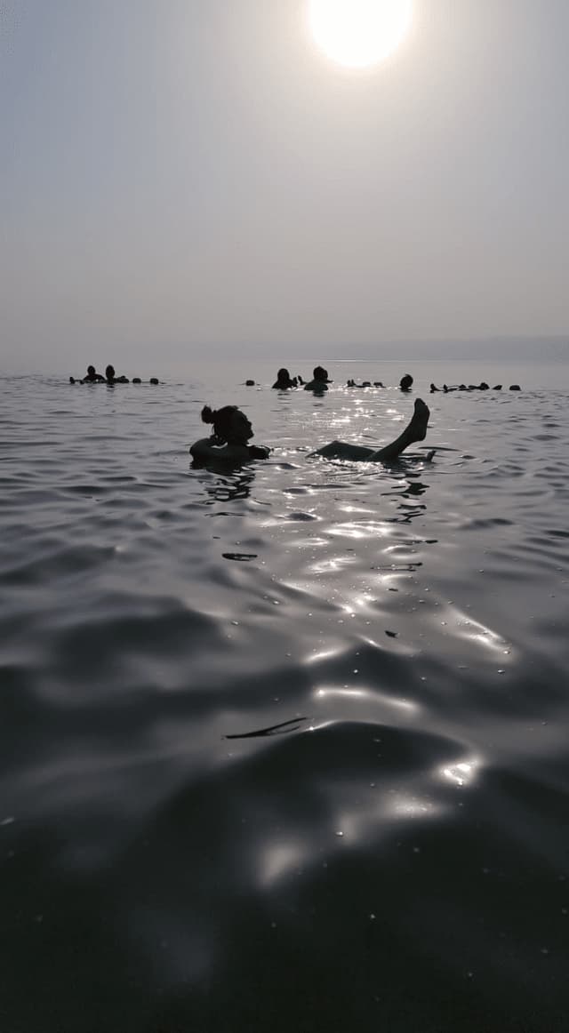 Sagome di un viaggio di gruppo WeRoad che galleggiano senza sforzo sulla schiena in acque calme sotto un sole luminoso e velato.