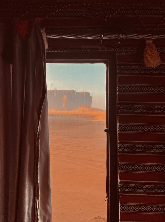 Una vista dall'interno di una tenda decorata, affacciata su un vasto paesaggio desertico con formazioni rocciose in lontananza.