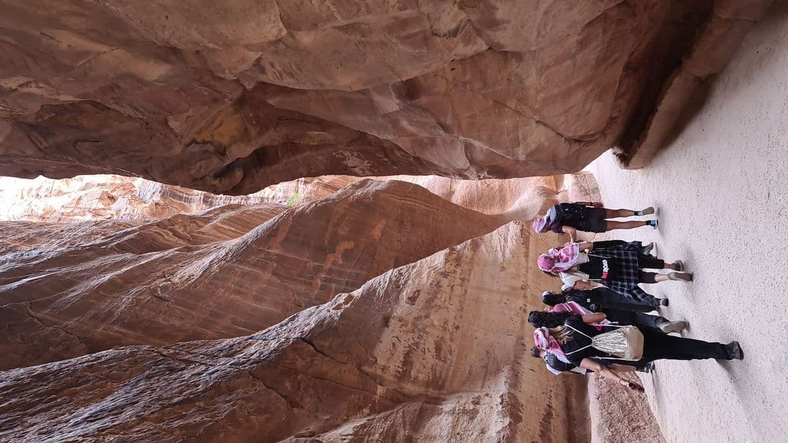 Un viaggio di gruppo WeRoad attraversa uno stretto canyon, circondato da alte pareti rocciose rosse a strati.