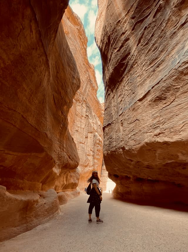 Da un'angolazione bassa, una donna si volta mentre si trova su un sentiero attraverso uno stretto canyon di arenaria dalle pareti imponenti.