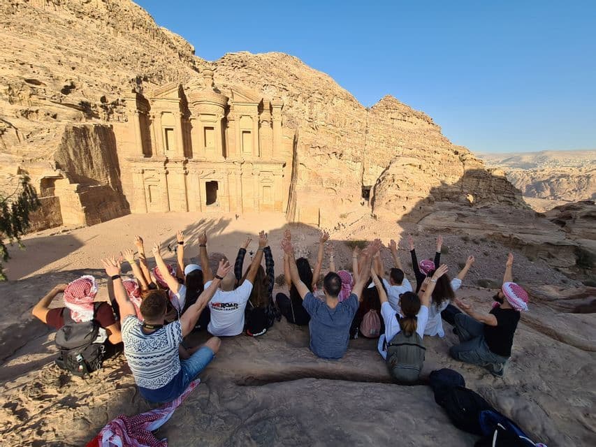 Un gruppo WeRoad è seduto di spalle alla fotocamera, con le braccia alzate verso un grande tempio scavato in una montagna di arenaria.