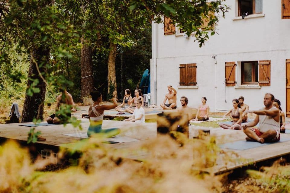 Un viaje en grupo de WeRoad participa en una clase de yoga al aire libre en una terraza de madera y césped junto a una casa.