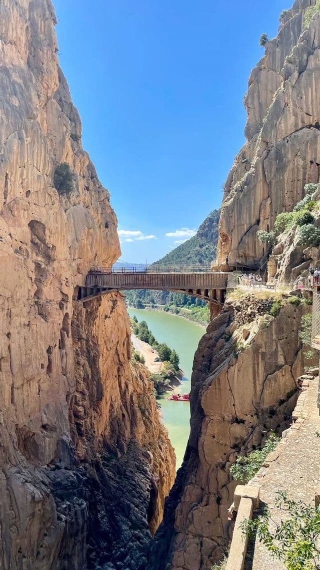 Un viaggio di gruppo WeRoad attraversa un ponte che sovrasta un canyon profondo con una stretta passerella scavata nella parete rocciosa.
