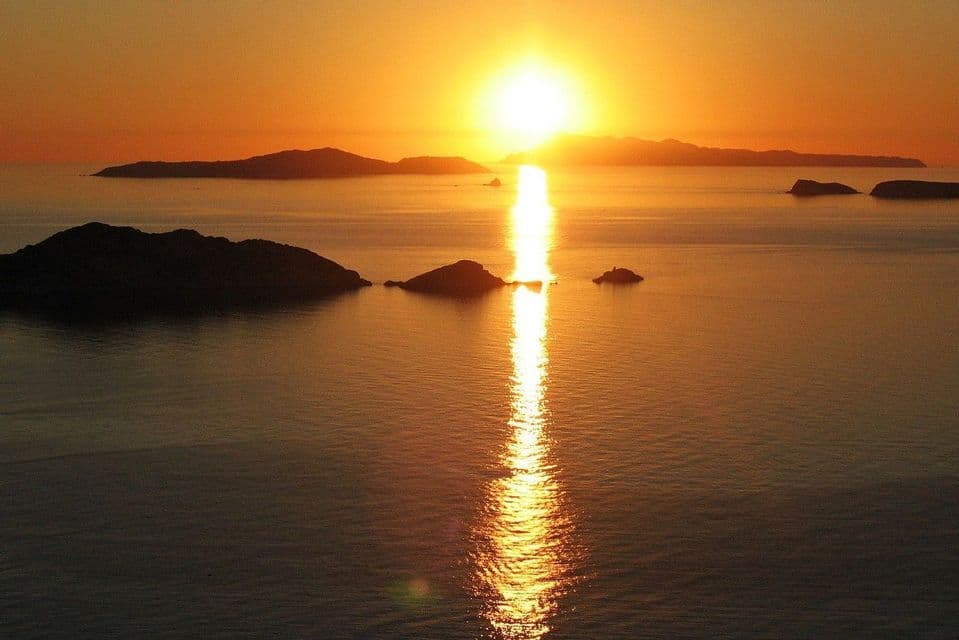 Il sole tramonta sull'oceano, proiettando un riflesso dorato sull'acqua con isole sagomate all'orizzonte.