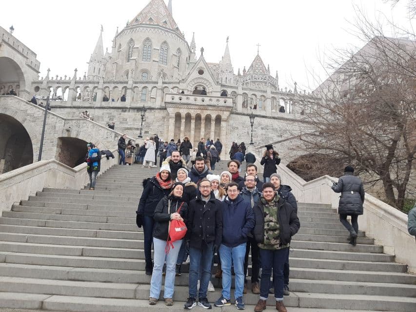 Un groupe WeRoad en voyage pose pour une photo sur un grand escalier en pierre devant un bâtiment historique avec des tours.