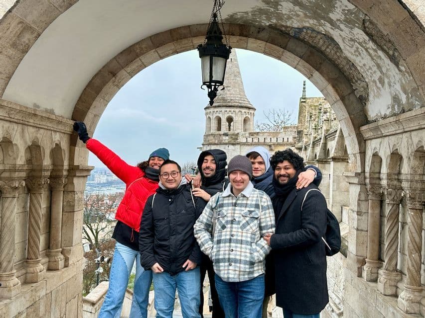 Un voyage de groupe WeRoad de six personnes souriant pour une photo sous une arche en pierre, avec une tour historique en arrière-plan.