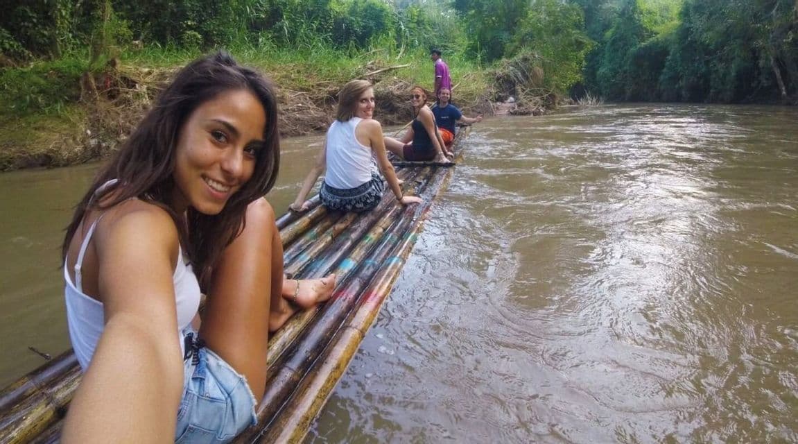 Une femme prend un selfie avec son groupe WeRoad, flottant sur un radeau en bambou le long d'une rivière à la végétation luxuriante.