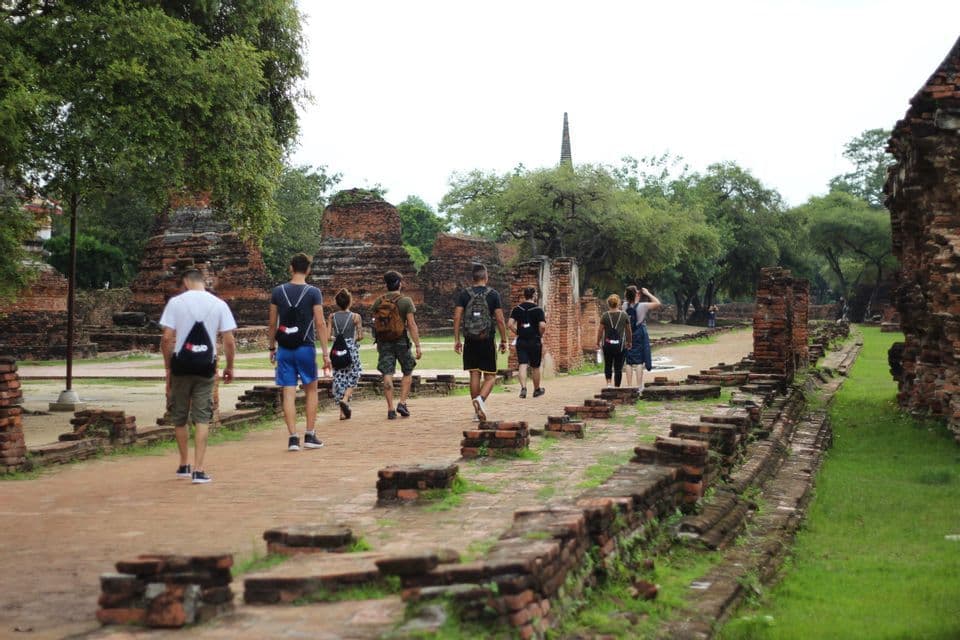 Un voyage de groupe WeRoad se promène le long d'un chemin de briques entouré d'anciennes ruines de temples et d'arbres verts.
