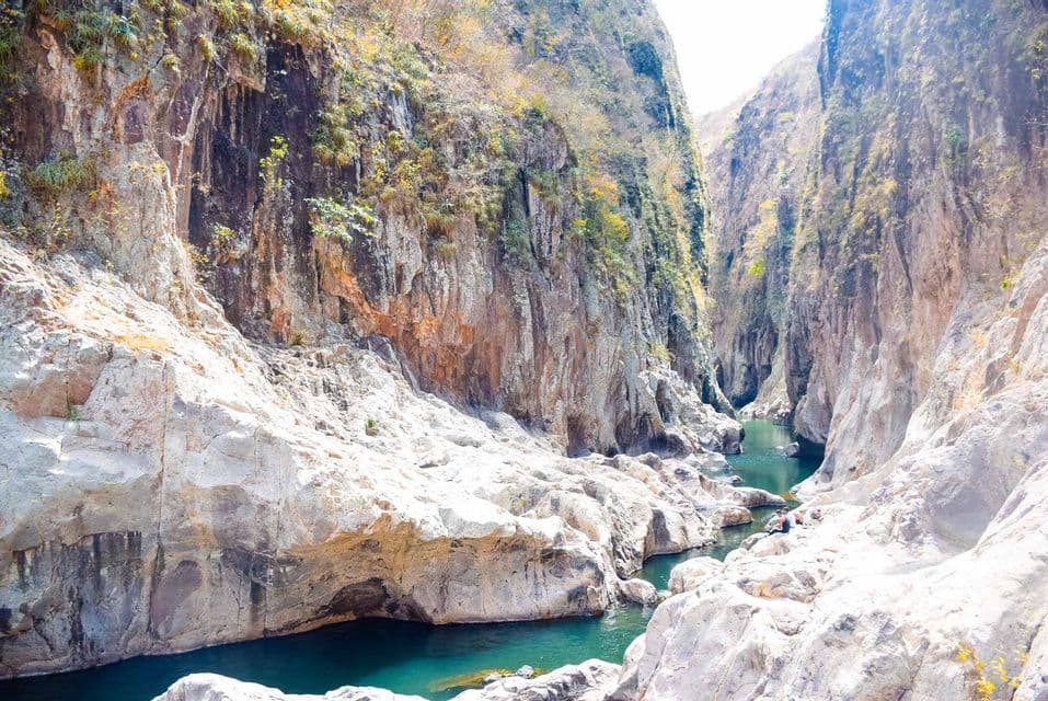 Ein türkisfarbener Fluss fließt durch eine tiefe Schlucht mit steilen, felsigen Wänden, wo sich einige Leute einer WeRoad Gruppenreise auf den sonnengebleichten Felsen ausruhen.