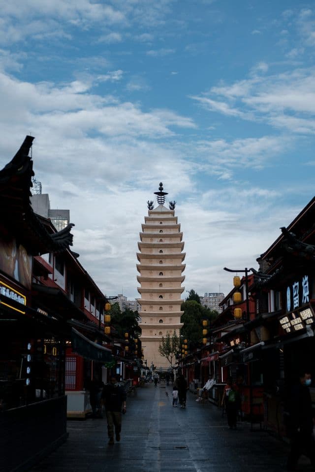 Una pagoda alta e a più livelli si erge alla fine di una strada lastricata fiancheggiata da edifici tradizionali sotto un cielo nuvoloso.
