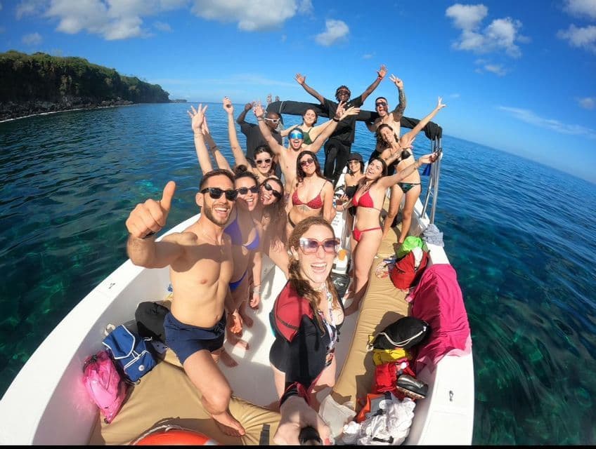 Un gruppo WeRoad in costume si scatta un selfie su una barca, in acqua azzurra sotto un cielo parzialmente nuvoloso.