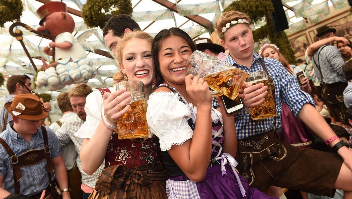 Un viaggio di gruppo WeRoad con persone in abiti tradizionali che sorridono e brindano con grandi boccali di birra in una tenda affollata e festosa.