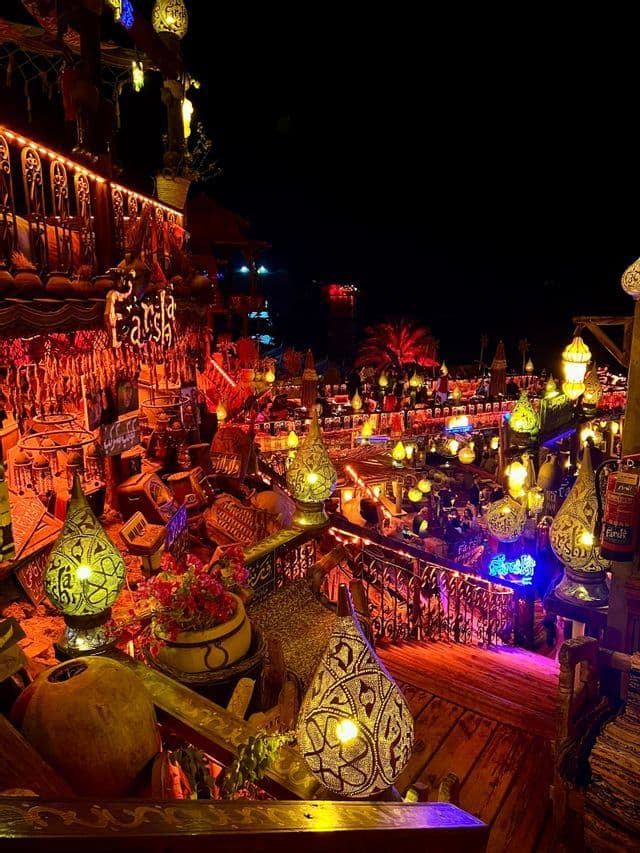 Un ambiente esterno su più livelli illuminato di notte da decine di lampade e lanterne ornate e colorate