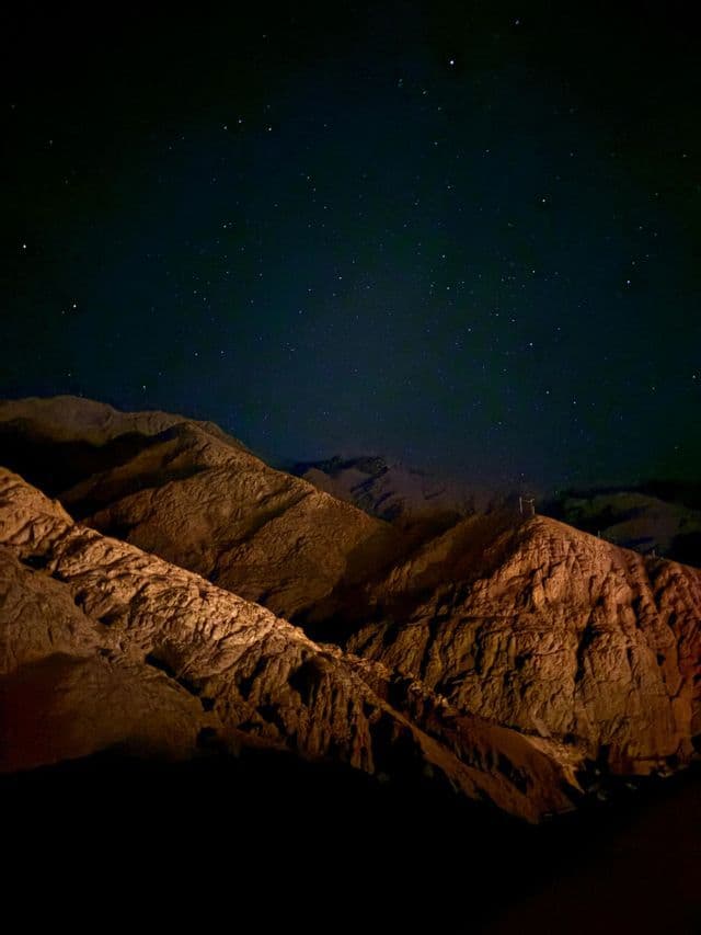 Montagne aspre illuminate da una luce calda contro un cielo notturno scuro e stellato