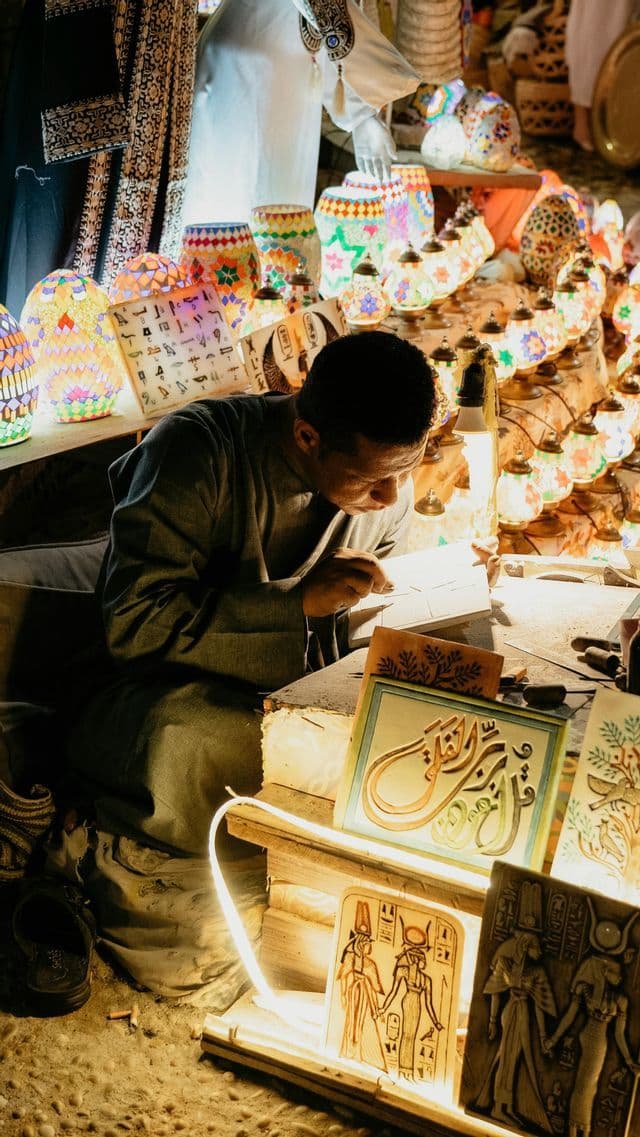 Un artigiano disegna con cura su una tavoletta in una bancarella del mercato, circondato da lampade a mosaico colorate e arte geroglifica.