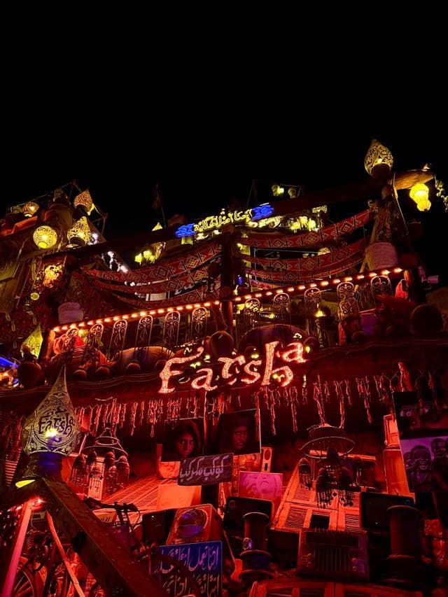 Un locale chiamato 'Farsha' è illuminato a giorno con luci rosse, lanterne tradizionali e tessuti a motivi, contro un cielo notturno scuro.