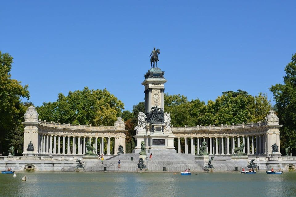 Un imponente monumento con statua equestre e un grande colonnato sorge accanto a un lago con persone che remano in piccole barche.