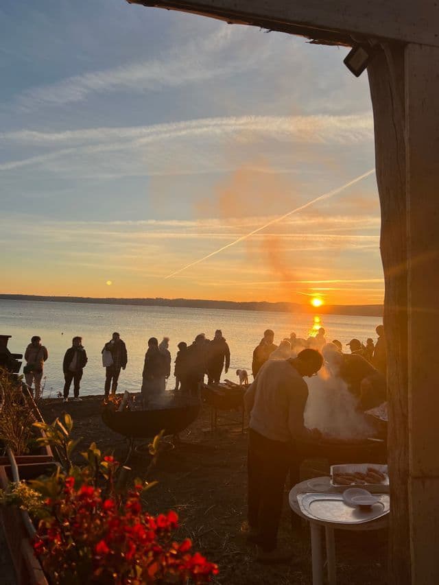 I partecipanti a un viaggio di gruppo WeRoad preparano una grigliata in riva al mare al tramonto.