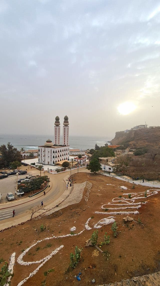 Eine Luftaufnahme einer Küstenstadt mit einer weißen Moschee und zwei Minaretten direkt am Meer unter einem diesigen Himmel.