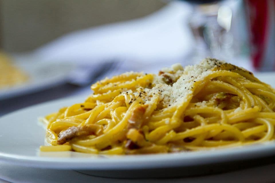 A close-up of a plate of spaghetti carbonara, garnished with grated cheese and black pepper.