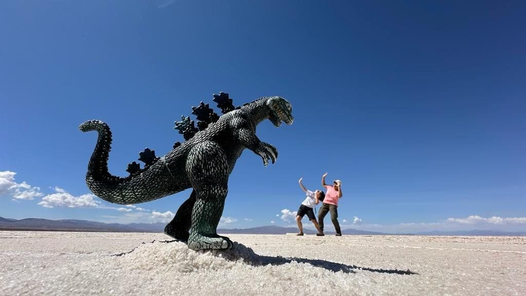 Una foto en perspectiva forzada muestra a dos personas de un viaje en grupo de WeRoad huyendo de un Godzilla de juguete en un salar.