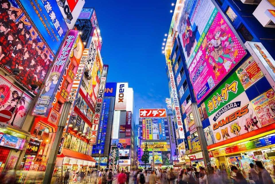 Eine belebte Stadtstraße bei Dämmerung, aus der Froschperspektive aufgenommen, gesäumt von hohen Gebäuden mit farbenfrohen, beleuchteten Schildern und japanischer Schrift.