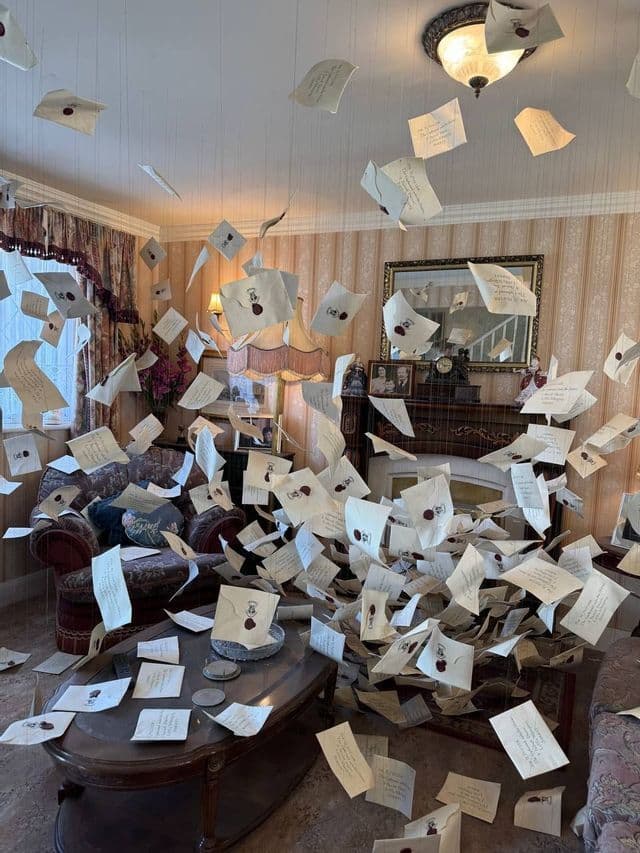 Centinaia di lettere con sigilli di ceralacca rossa sono sospese nell'aria, riempiendo un salotto in stile vintage.