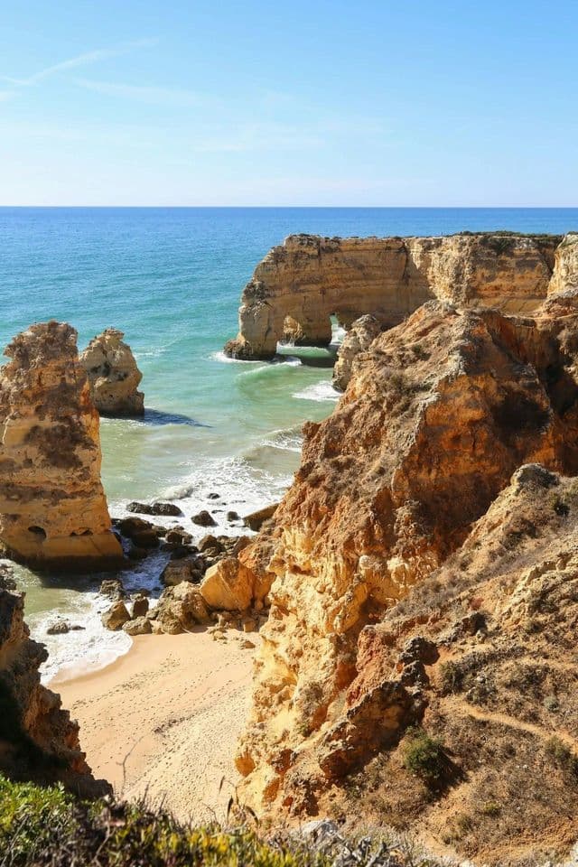 Ein Blick von einer hohen Klippe mit Blick auf einen abgelegenen Sandstrand und felsige Meeresbögen im türkisfarbenen Ozean.