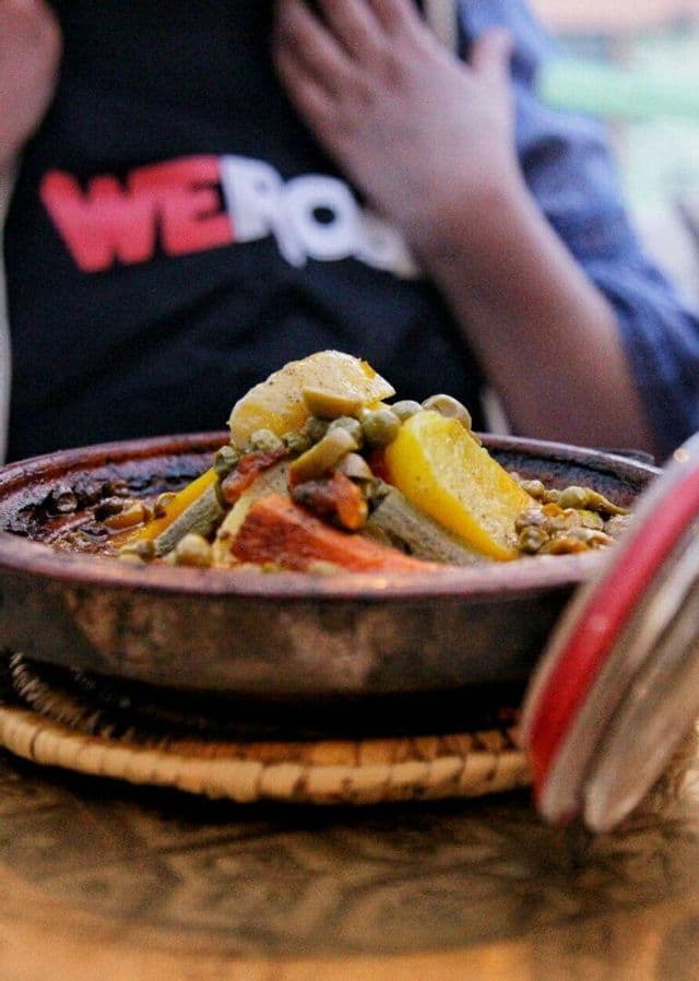 Nahaufnahme einer Gemüse-Tajine in einem Tontopf, mit einer Person einer WeRoad-Gruppenreise im Hintergrund.
