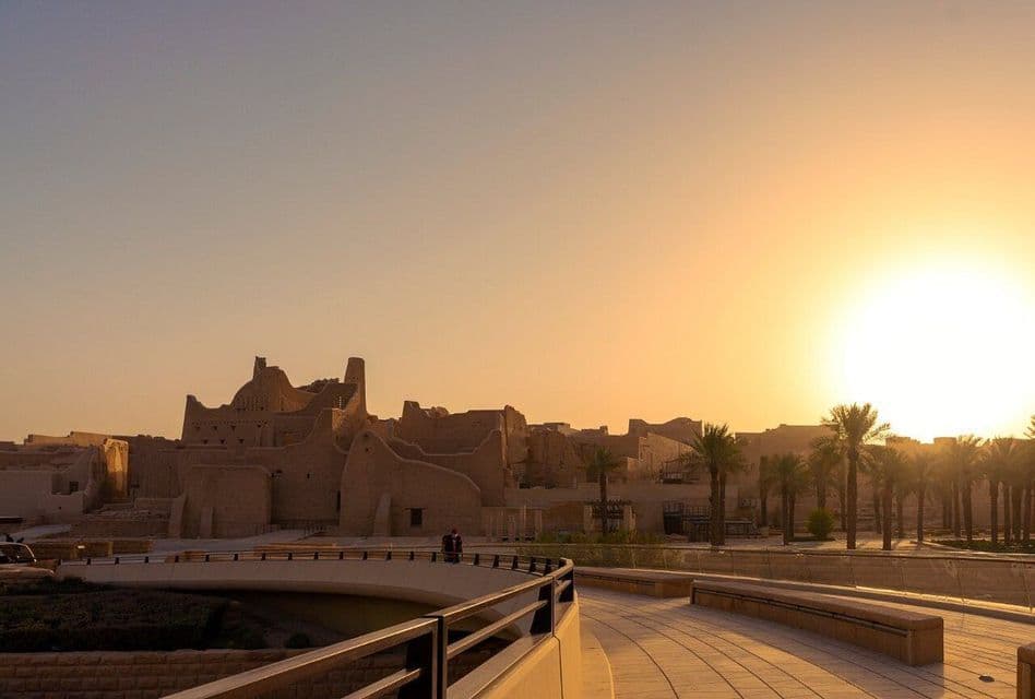 D'anciens bâtiments en briques de terre et des palmiers sont illuminés par le soleil couchant sous un ciel dégagé.
