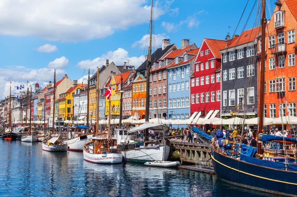 Bunte Gebäude säumen einen Kanal, an dem an einem sonnigen Tag zahlreiche Boote und Segelboote festgemacht sind.