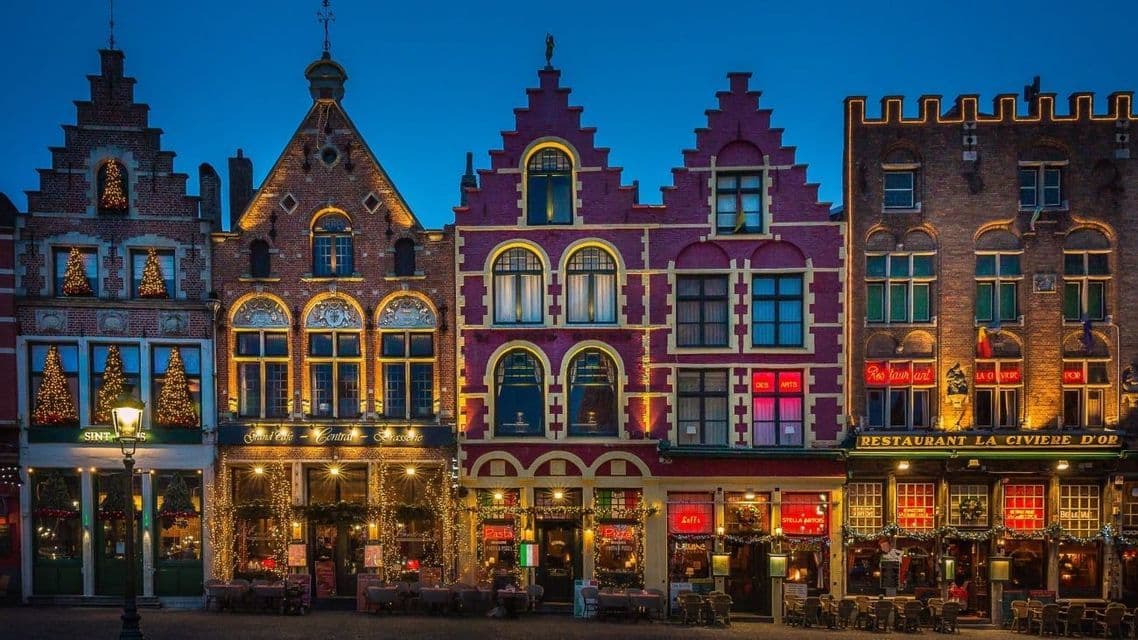 Une rangée de bâtiments historiques colorés aux pignons à redents, décorés de lumières de Noël et illuminés au crépuscule.