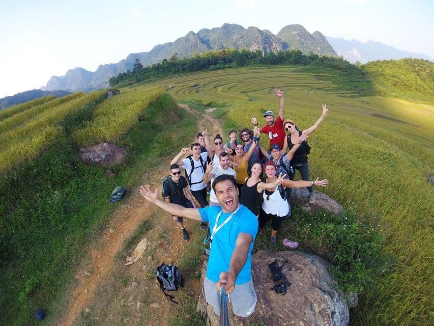 Un groupe WeRoad prend un selfie sur un sentier surplombant des collines et montagnes verdoyantes en terrasses sous un ciel clair.