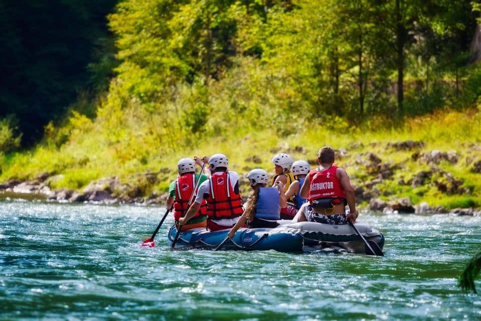 A WeRoad group trip wearing helmets and life vests while rafting down a river, with a tree-lined shore in the background.