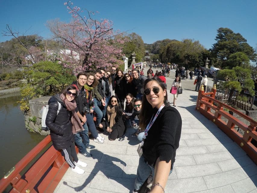 A WeRoad group trip poses for a selfie on a red bridge in a park with cherry blossoms.