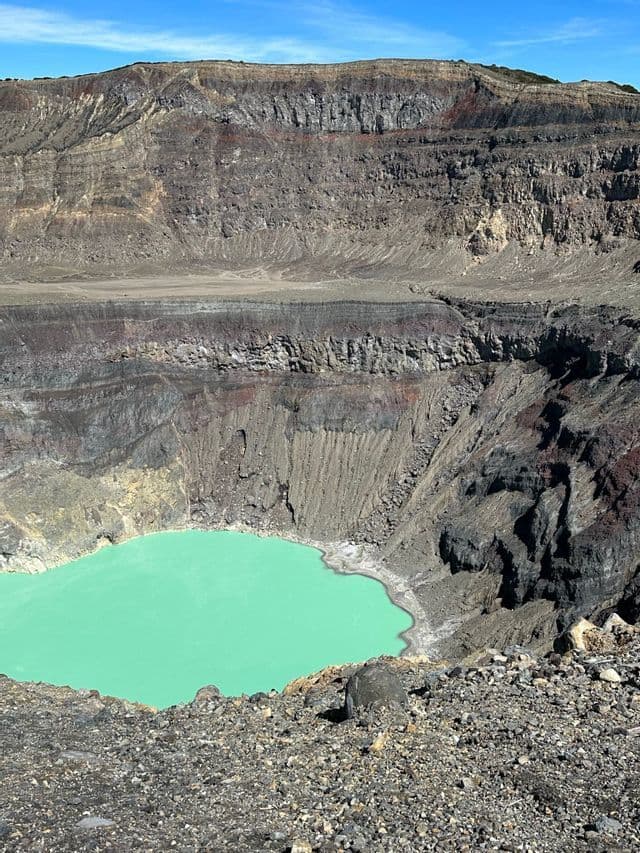 Ein Blick von oben auf einen türkisfarbenen See im Vulkankrater, umgeben von steilen, geschichteten Felswänden.