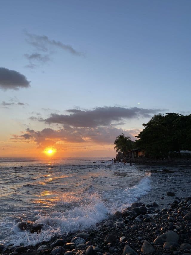 Die Sonne geht über dem Ozean unter, mit Wellen, die an einem felsigen Ufer brechen, wo sich eine WeRoad-Gruppenreise versammelt hat.