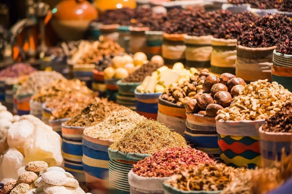 Vue rapprochée de diverses épices, herbes et noix exposées dans des sacs rayés colorés sur un étal de marché.