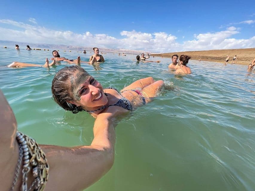 Une femme souriante, le visage couvert de boue, prend un selfie tout en flottant dans l'eau lors d'un voyage de groupe WeRoad.