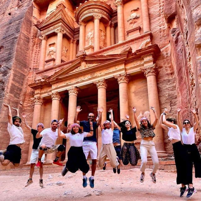 Un viaje en grupo de WeRoad saltando para una foto frente a un gran templo antiguo excavado en un acantilado de roca roja.