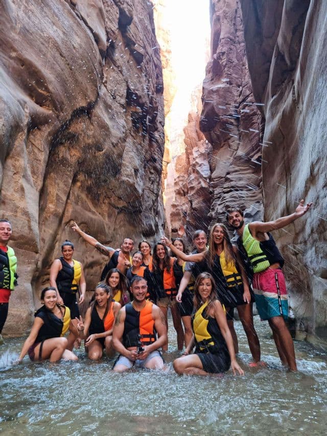 A WeRoad group trip wearing life vests poses for a photo while splashing in the water inside a narrow canyon.