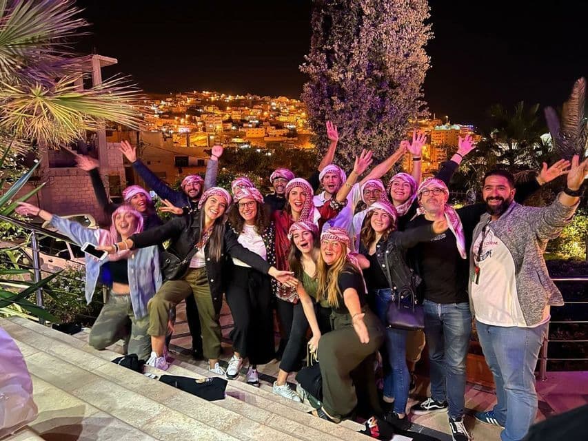 Un gruppo WeRoad in viaggio, indossando foulard tradizionali, posa per una foto su delle scale di notte, con un paesaggio urbano illuminato sullo sfondo.