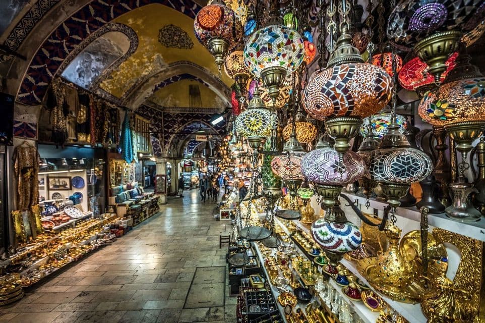 Des lanternes en mosaïque colorées pendent du plafond voûté d'un marché couvert animé, rempli de stands de souvenirs.